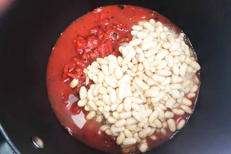 Horizontal image of white beans and fire-roasted tomatoes in a black pot.