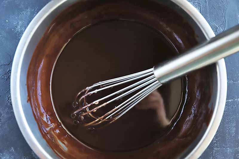 Horizontal image of a whisk in a bowl with melted chocolate.