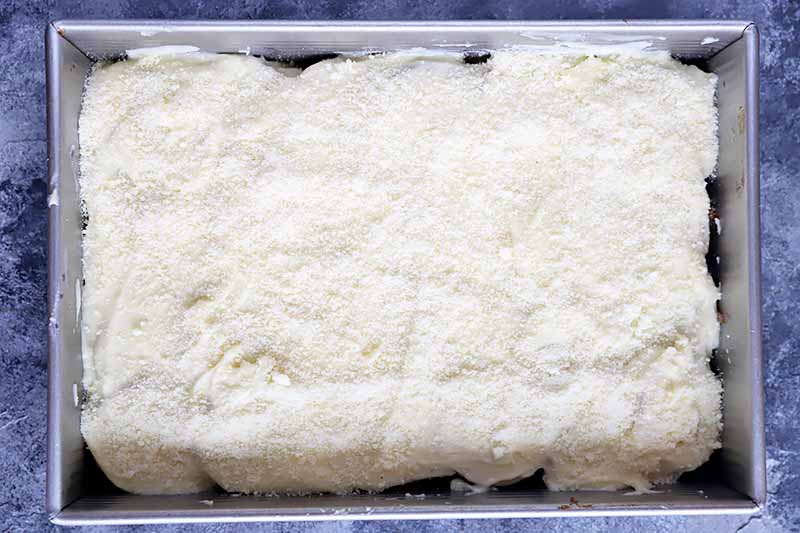 Horizontal image of a layer of mornay sauce spread in a baking dish topped with grated cheese.