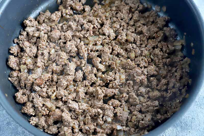 Horizontal image of cooked ground meat in a skillet.
