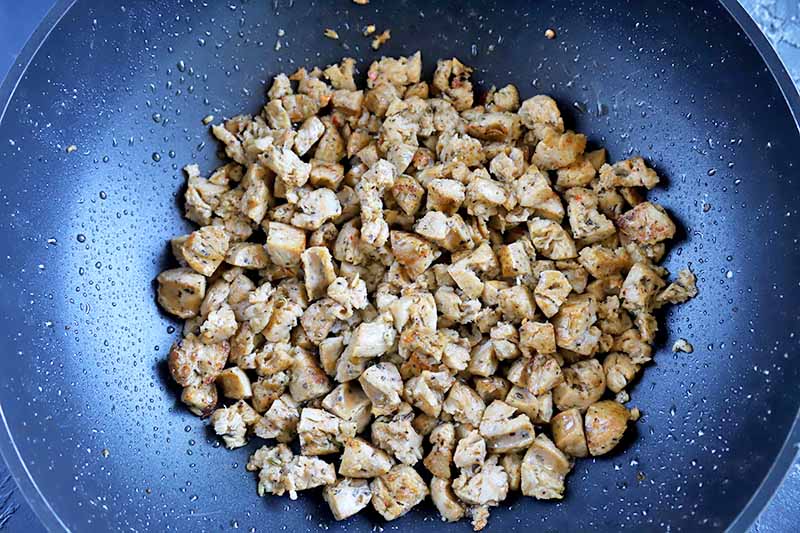Horizontal image of cooked crumbled sausage in a wok with oil.