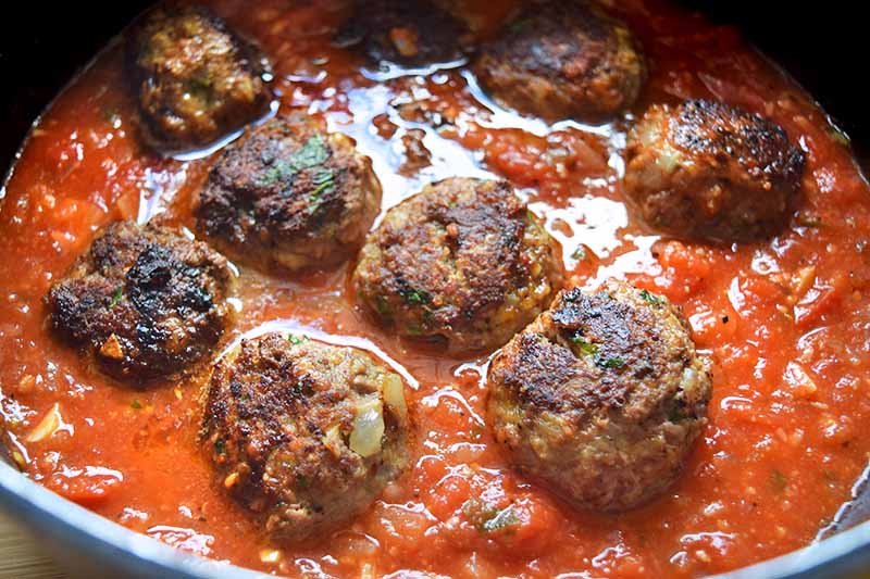 Oblique overhead image of eight meatballs in marinara sauce, in a large frying pan.
