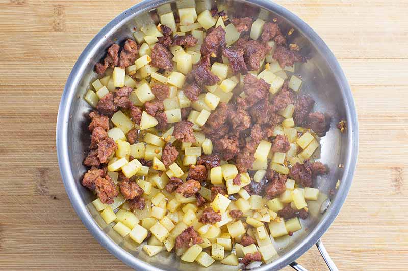 Horizontal image of diced potatoes and crumbled chorizo mixed together in a pan.