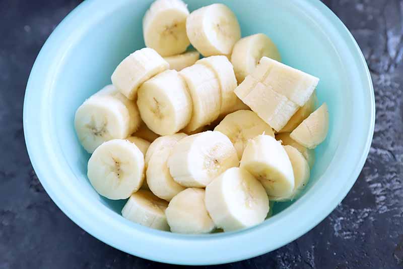 Horizontal image of sliced bananas in a blue bowl.