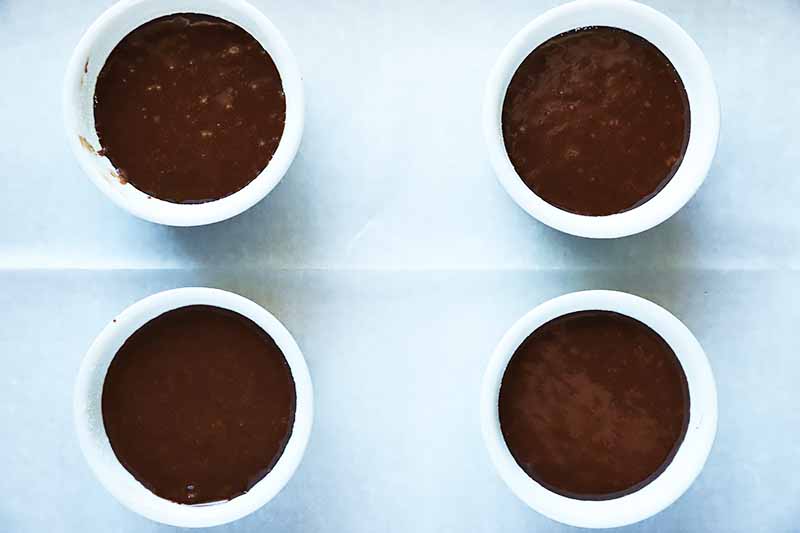 Horizontal image of four ramekin dishes filled with a cocoa batter.