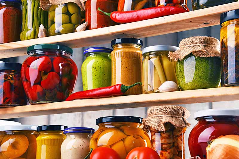 Horizontal image of wooden shelves full of assorted jarred vegetables and sauces.