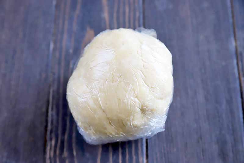 Horizontal image of a mound of dough tightly wrapped in plastic wrap.