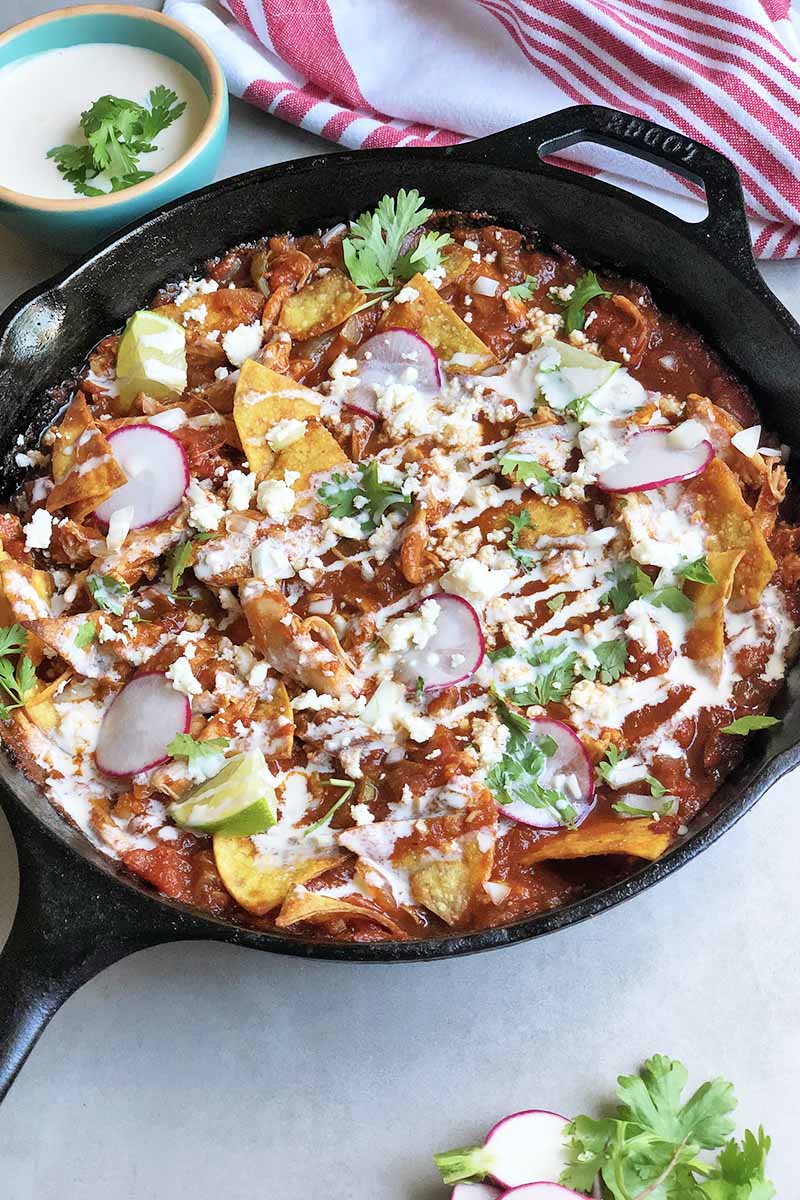 Vertical image of a cast iron skillet with chilaquiles and shredded poultry.
