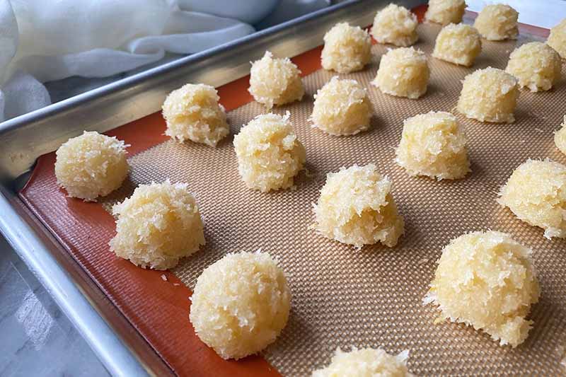 Horizontal image of small mounds of coconut macaroon batter on a baking sheet with a silicone mat.