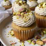 Horizontal image of cupcakes topped with vanilla icing and crushed nuts on a white plate.
