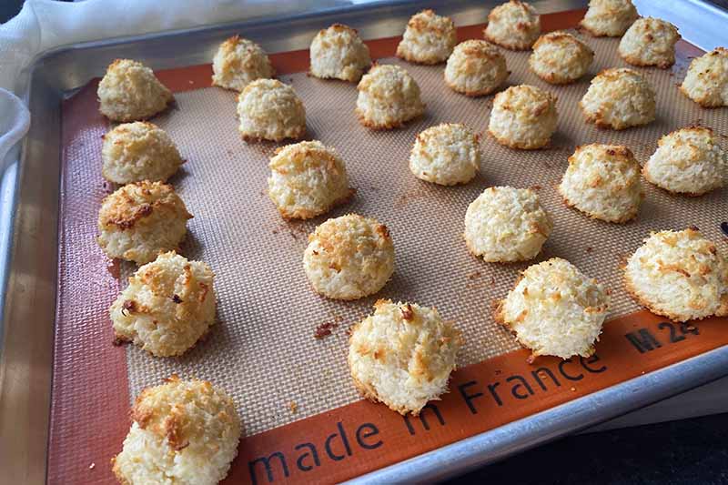 Horizontal image of baked macaroons on a baking sheet lined with a silicone mat.