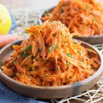 Horizontal image of two wooden bowls filled high with a carrot slaw on a roped placemat next to a lemon.