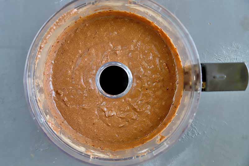 Horizontal top-down image of a thick brown batter in a food processor.