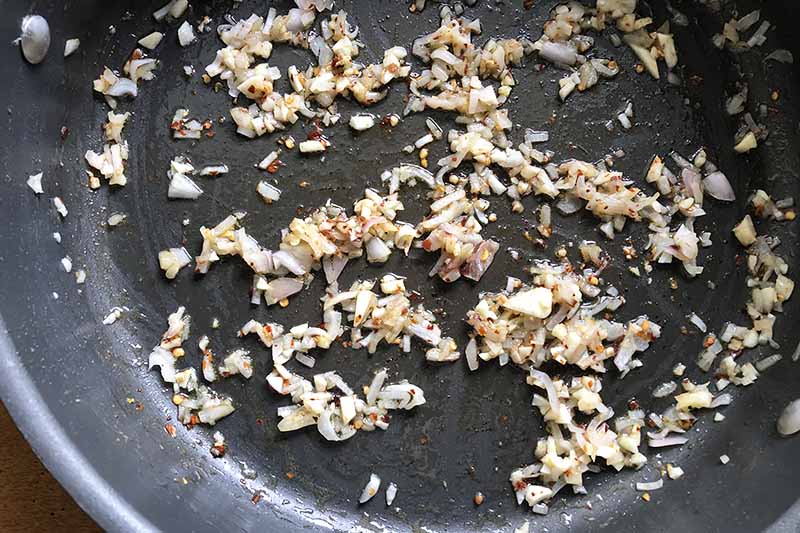 Horizontal image of sauteed shallots and garlic in a pan.