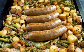 Horizontal image of four whole meat links in the middle of a tray with seasoned potatoes and beans.