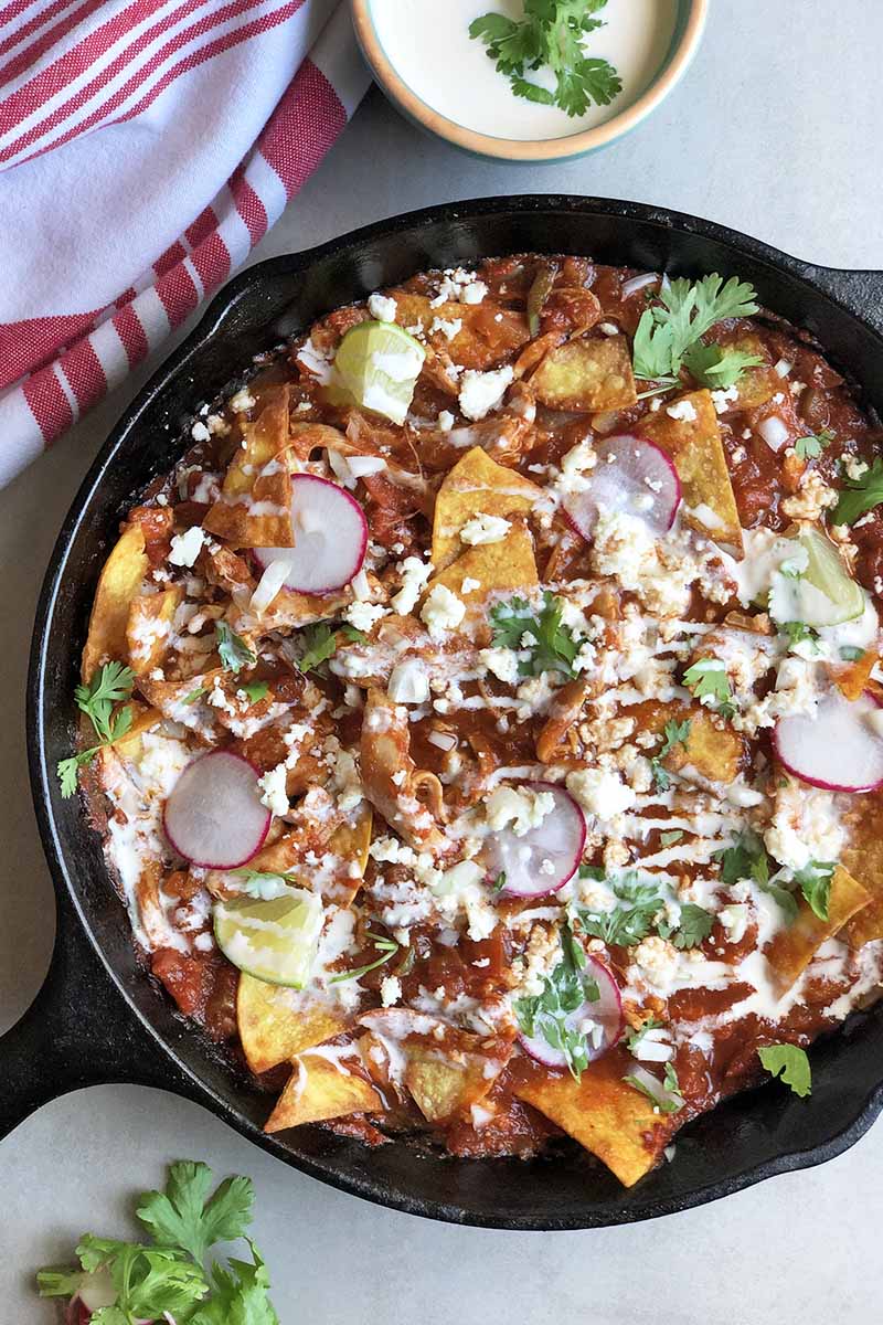 Vertical top-down image of a cast iron skillet with a saucy nacho dish with various toppings.