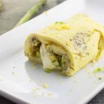 Horizontal image of half of a green vegetable and melted mozzarella cheese omelet on a white plate with a chive and lemon zest garnish.