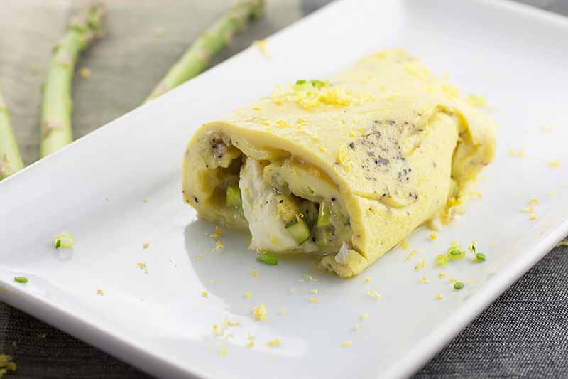 Horizontal image of half of a green vegetable and melted mozzarella cheese omelet on a white plate with a chive and lemon zest garnish.