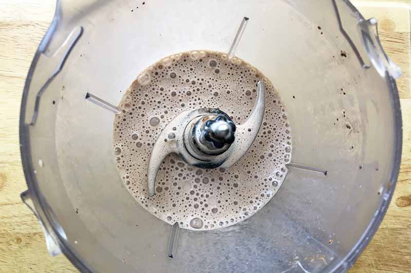 Horizontal image of a blender with a frothy brown liquid.