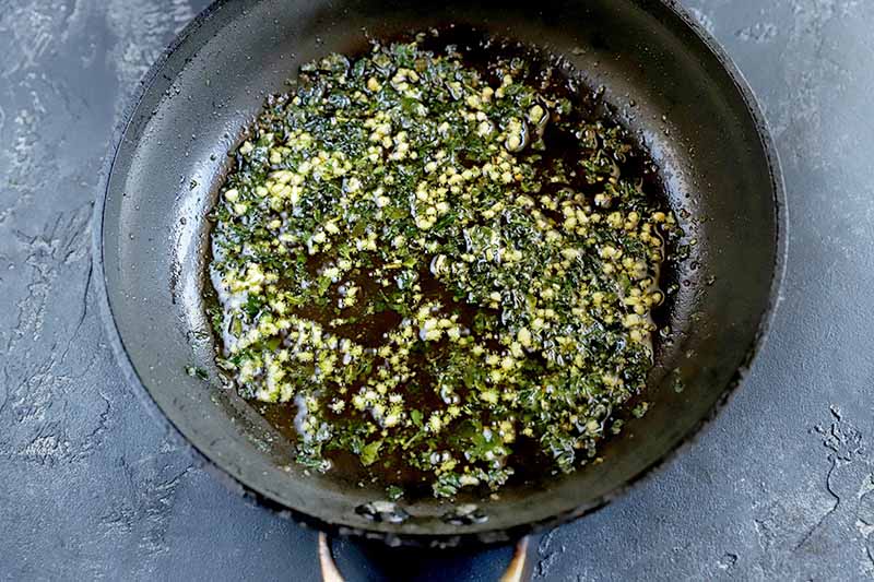 Horizontal overhead image of a nonstick saucepan filled about halfway with a lemon and herb sauce, on a gray surface.