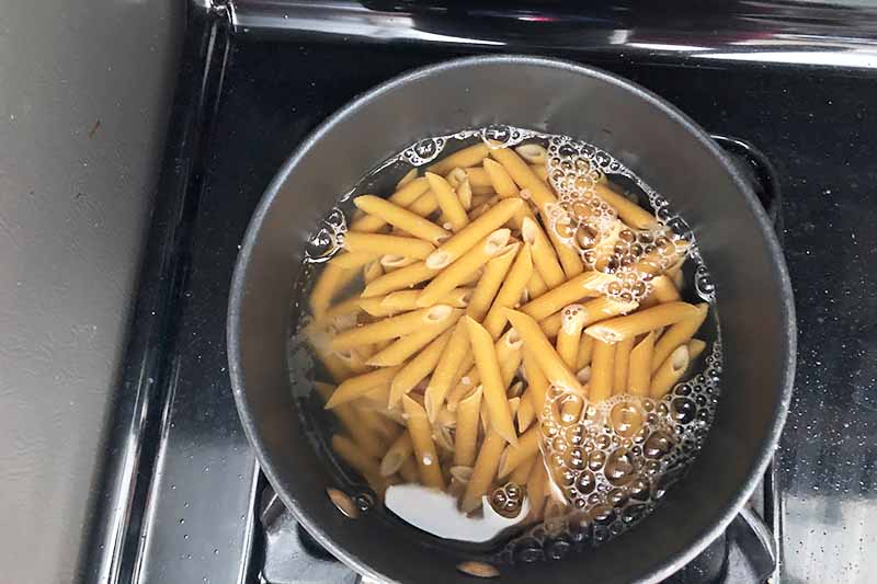 Horizontal image of cooking pasta in a pot on a stovetop.