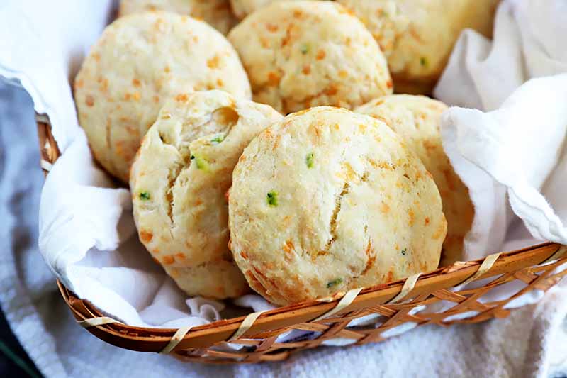 Horizontal image of a basket lined with a white towel filled with cheddar chive biscuits.