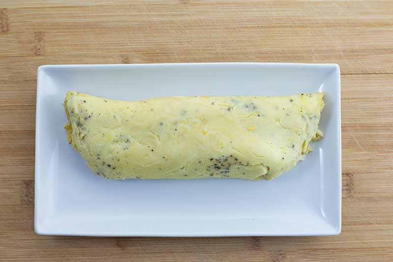 Horizontal image of a rolled omelet on a rectangular white dish on a wooden board.