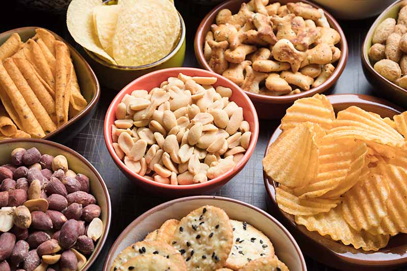 Horizontal image of bowls of various crunchy snack foods.