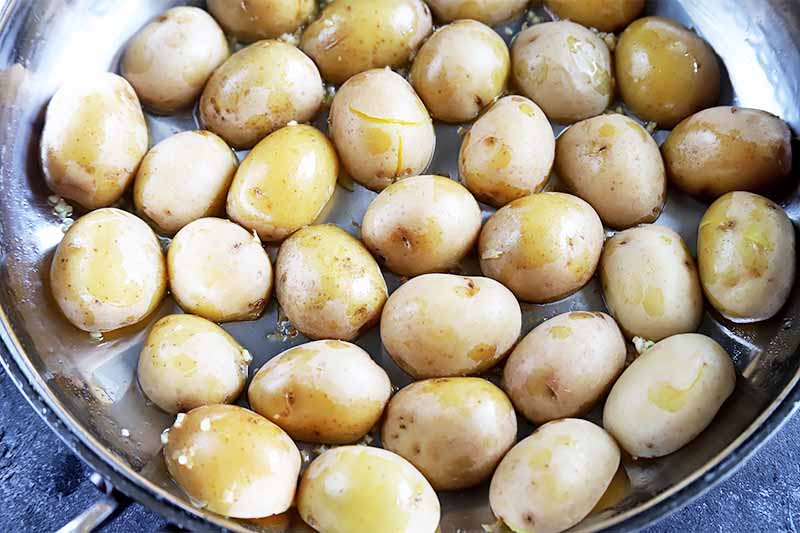Horizontal image of a pan with oil and uncooked halved spuds.