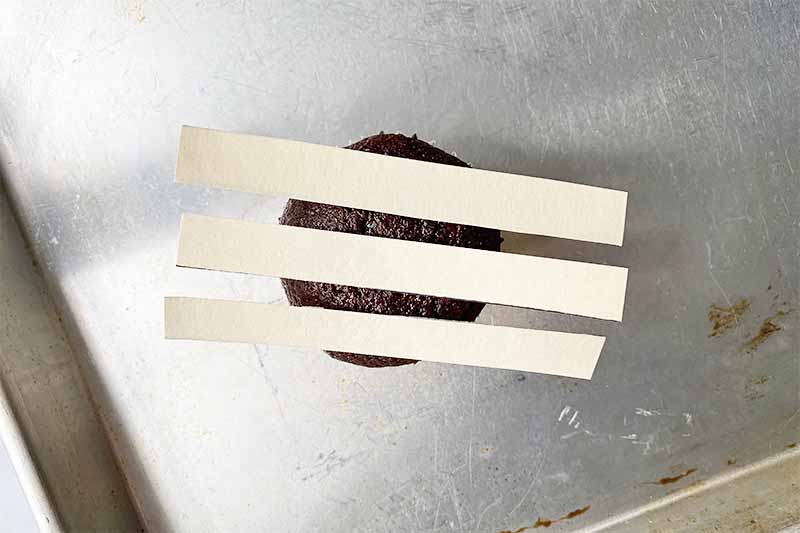 Horizontal image of three stripe stencils on top of a small, circular chocolate dessert on a baking sheet.