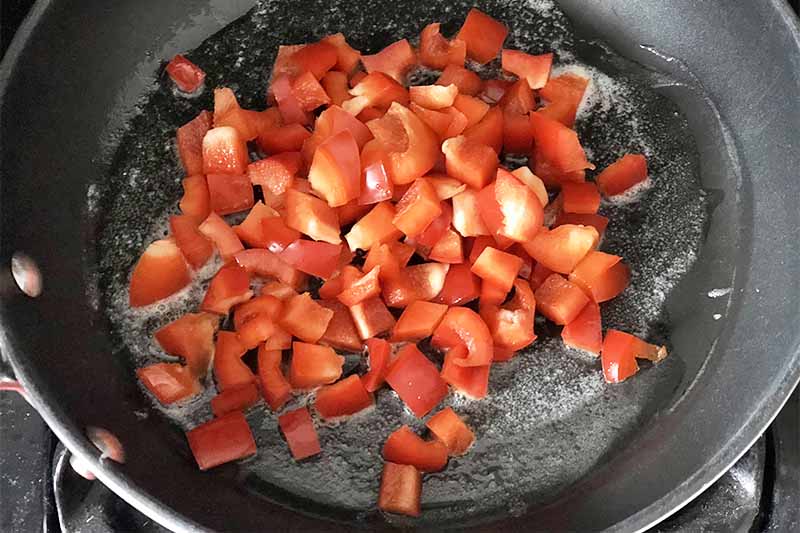 Horizontal image of chopped red peppers and oil in a black skillet.