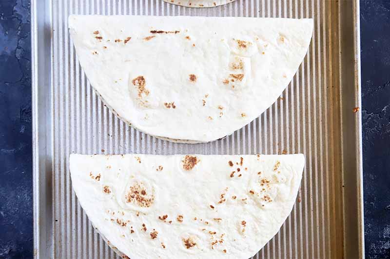 Horizontal image of two folded flour tortillas on a baking sheet.