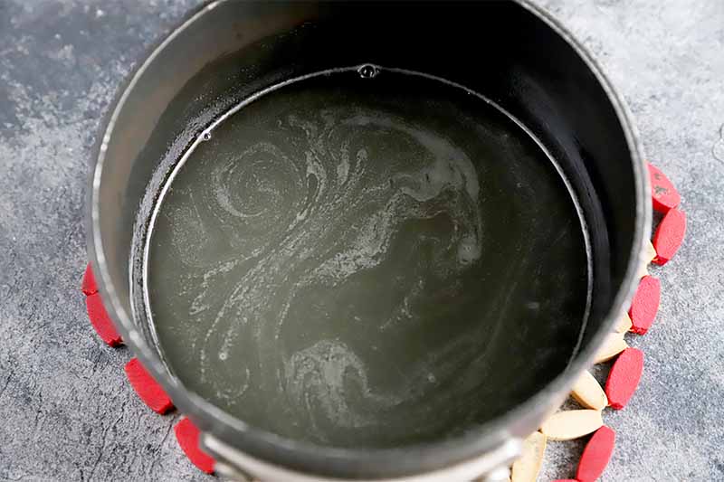 Horizontal image of a pot with a light yellow swirled liquid mixture on a gray surface.