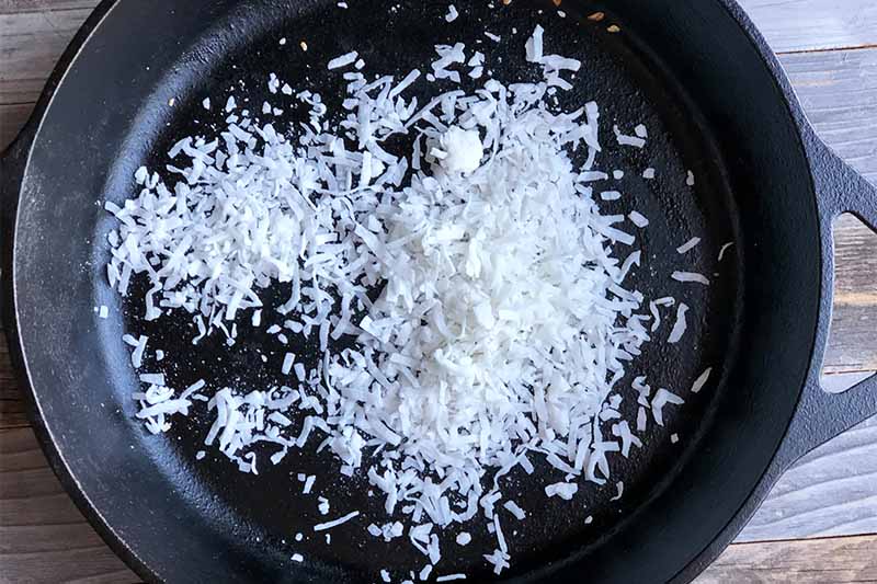 Horizontal image of toasting shredded coconut in a black skillet.