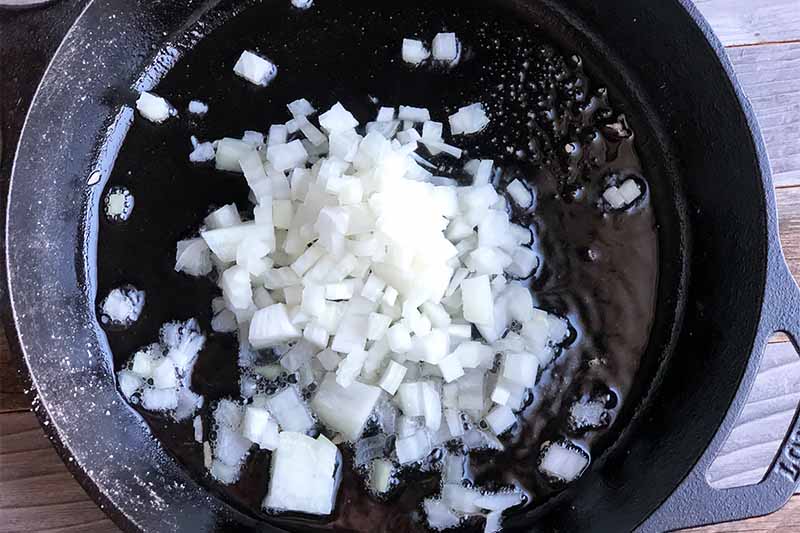 Horizontal image of diced onion in a black skillet.