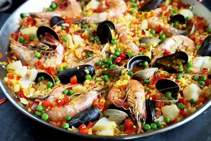 Horizontal image of a pan filled with paella and whole seafood.