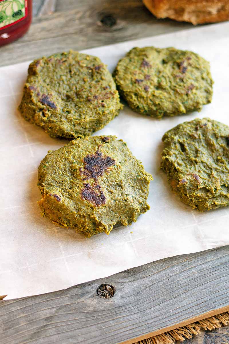 Vertical image of four cooked green patties on a sheet on a gray wooden surface.