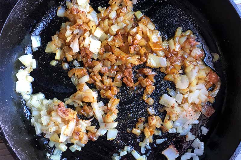 Horizontal image of cooked diced onions and spices in a skillet.