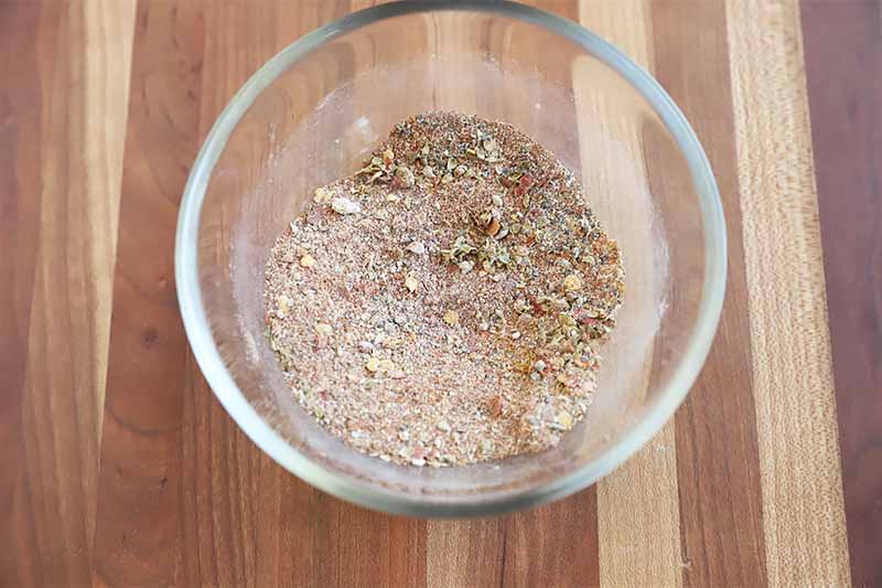 Horizontal image of a light spice mixture in a small glass bowl on a wooden table.