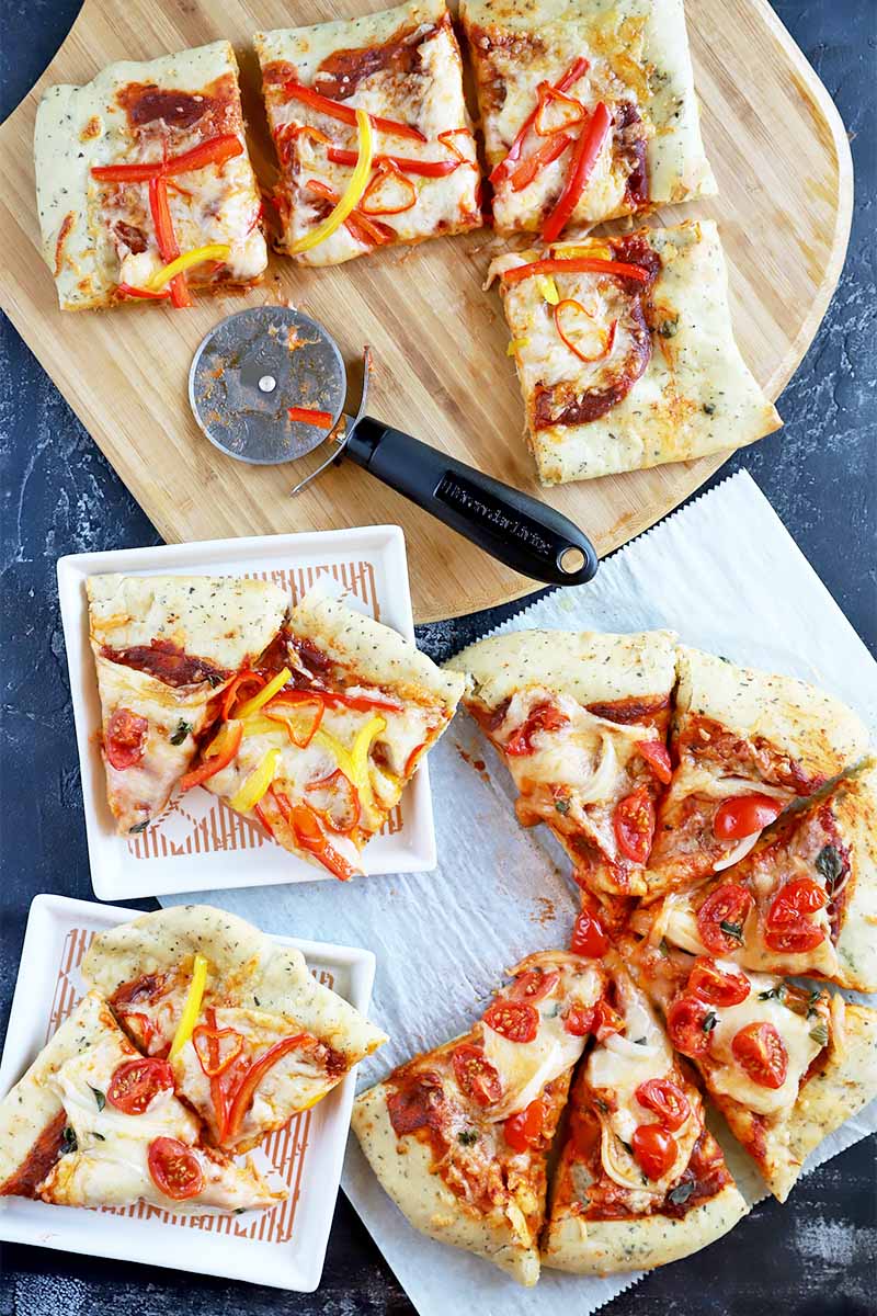 Vertical top-down image of assorted slices of pizza on white square plates, a wooden cutting board, and parchment paper.