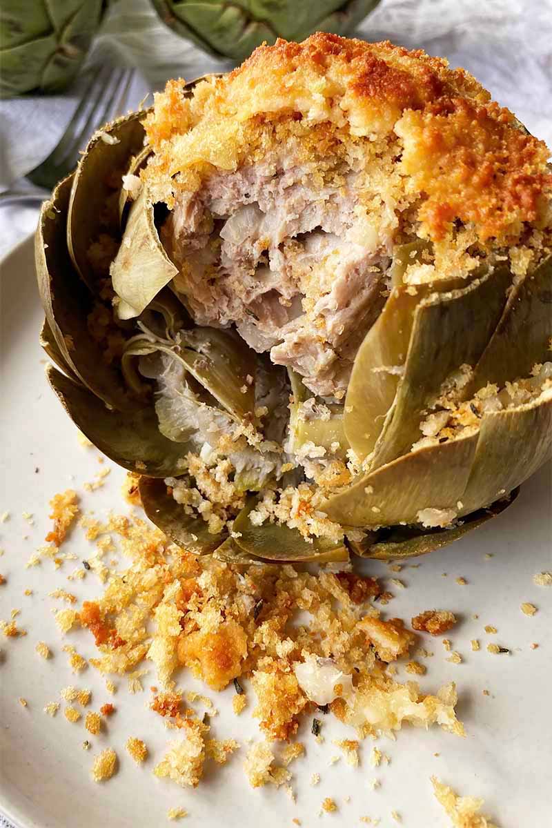 Vertical close-up image of the inside of a sausage-stuffed whole artichoke on a white plate, with crumbs scattered on the plate.