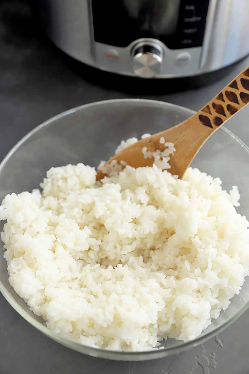 Vertical image of a bowl of cooked white grains with a wooden spoon.