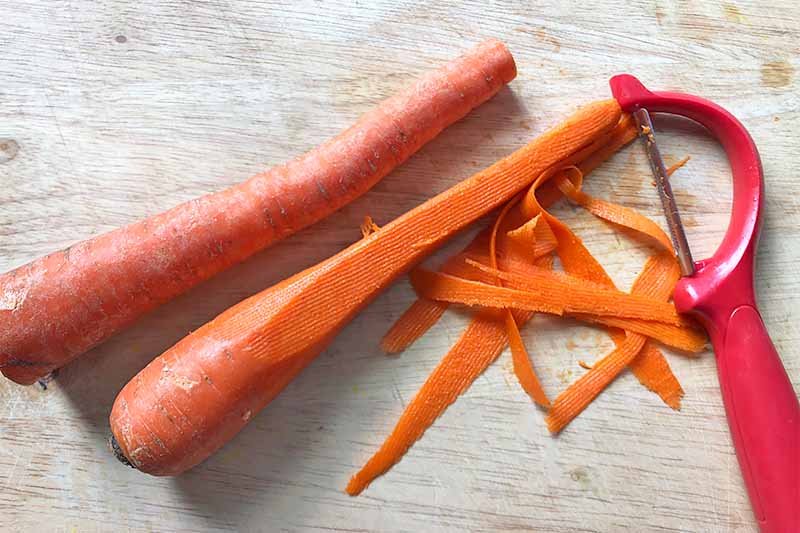 Horizontal image of whole carrots, a vegetable peeler, and some carrot ribbons.