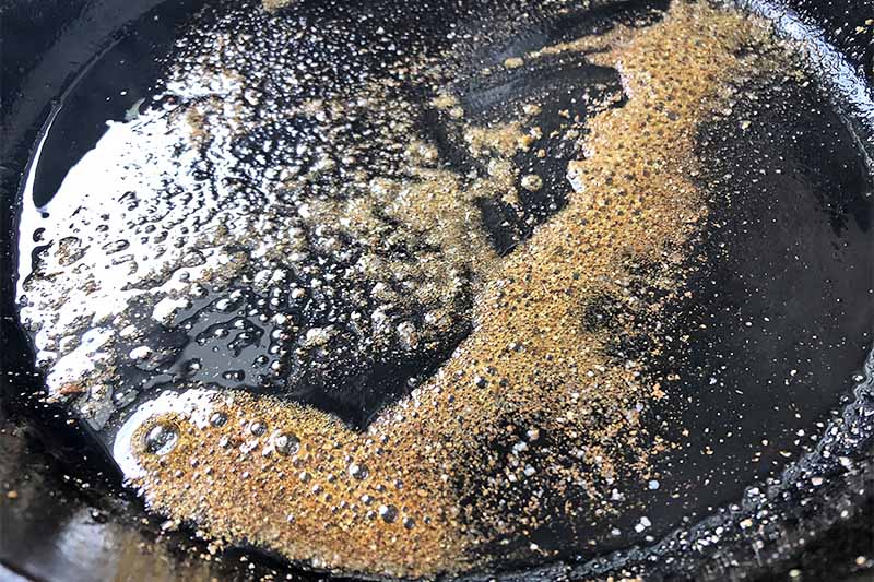 Horizontal image of cooking ground spices and oil in a black pan.
