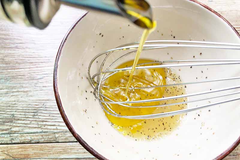 Horizontal image of whisking together oil with lemon juice in a white bowl.