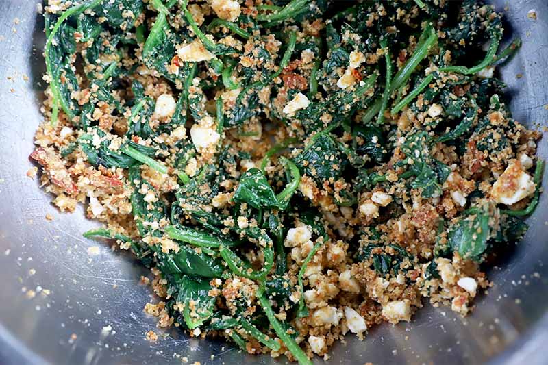Horizontal image of a mixture of spinach, feta, pesto, and breadcrumbs.