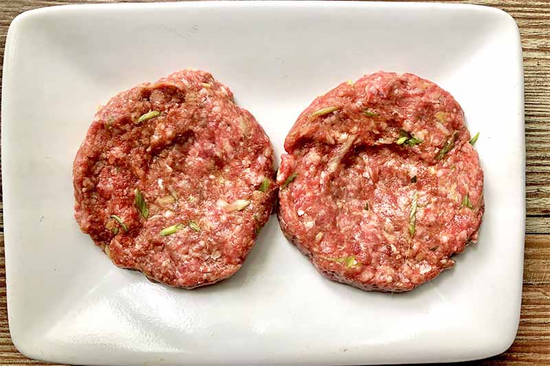 Horizontal image of two raw meat patties on a white plate.