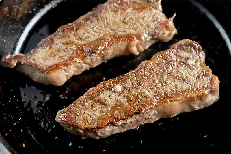 Horizontal image of two cooked steaks in a pan.