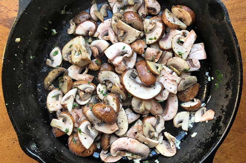 Horizontal image of cooking seasoned sliced mushrooms in a pan.
