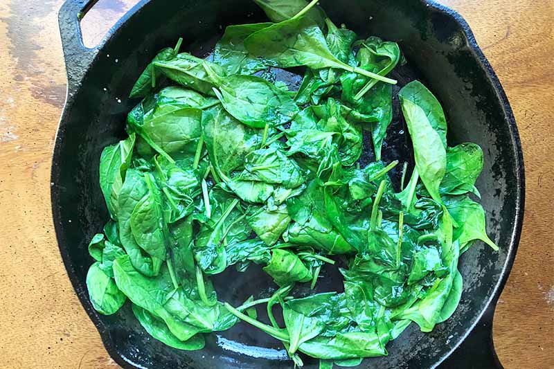 Horizontal image of cooking spinach in a skillet.